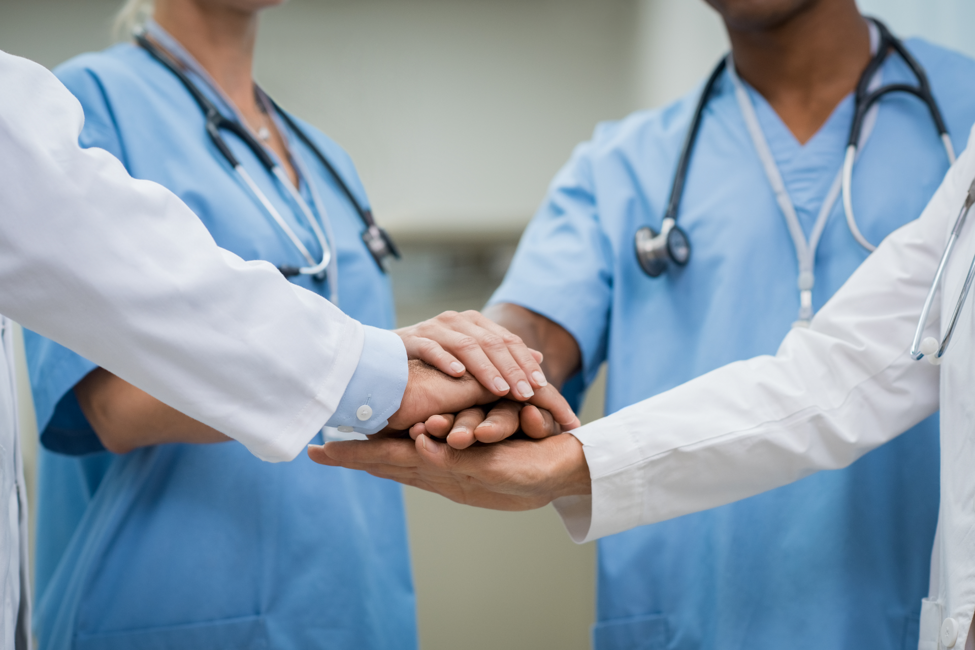 Medical team with hands stacked in a show of unity, wearing scrubs and white coats.