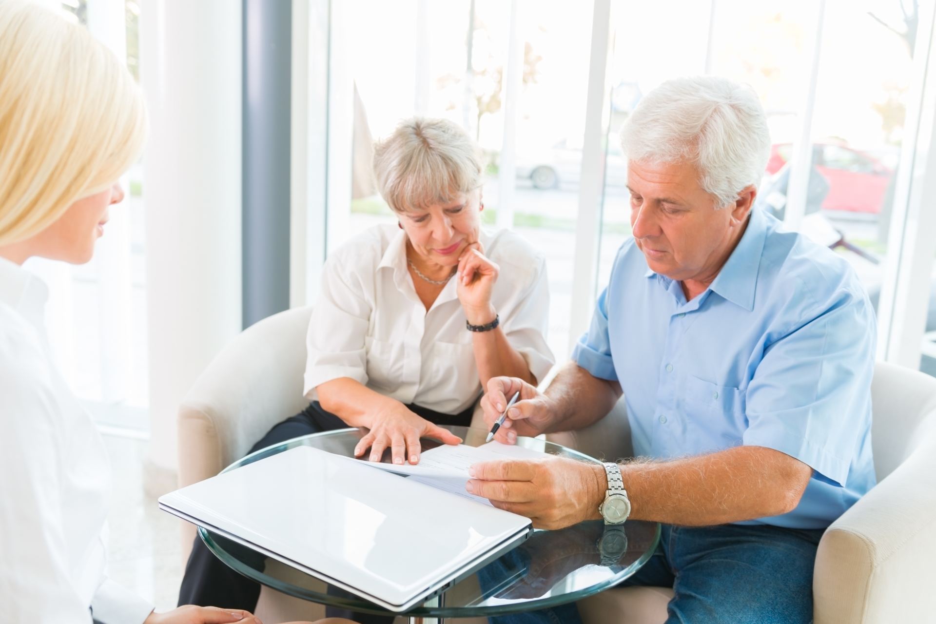 Older couple smiles while consulting with a person about documents in a home setting.