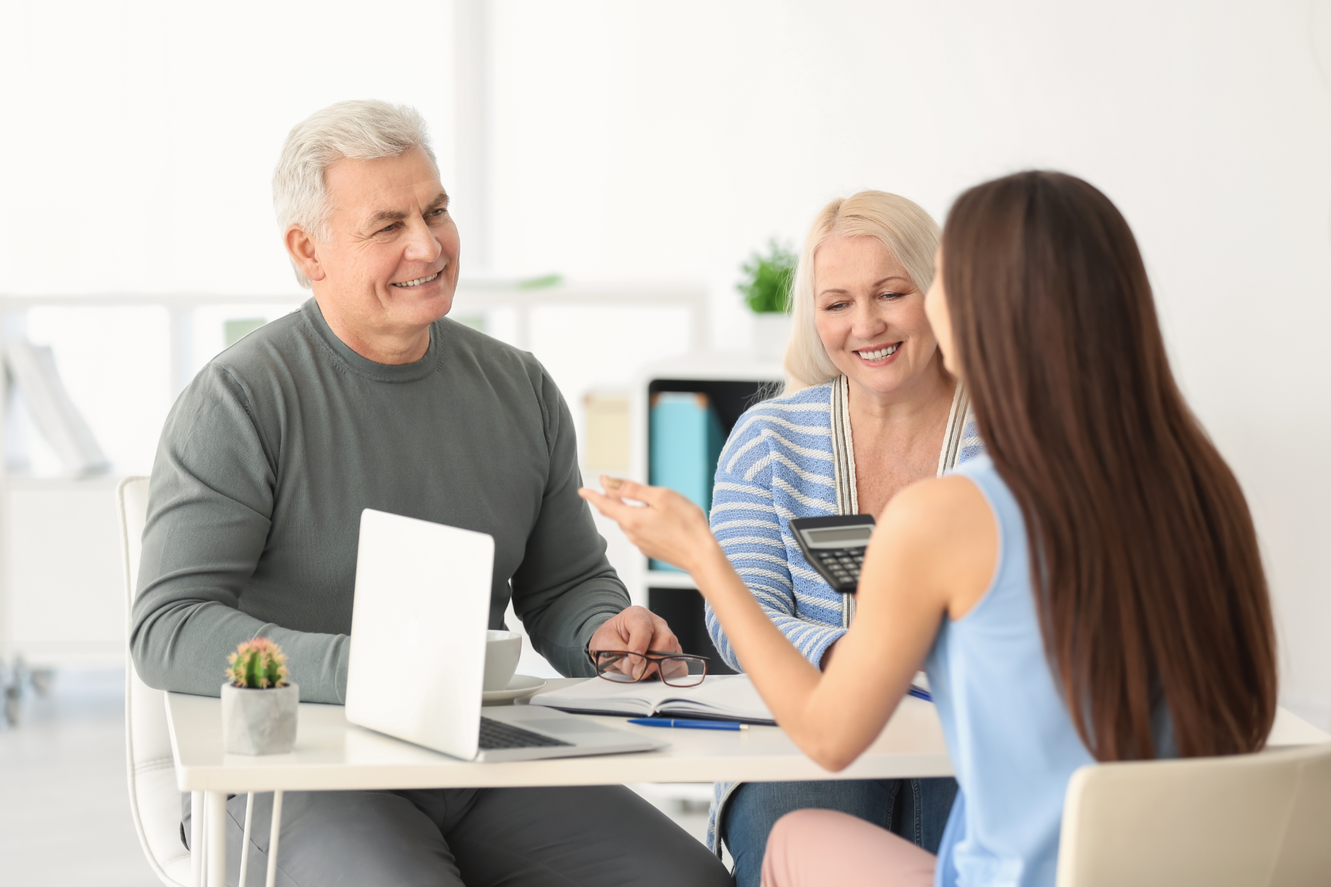 Older couple smiles while consulting with a person about documents in a home setting.