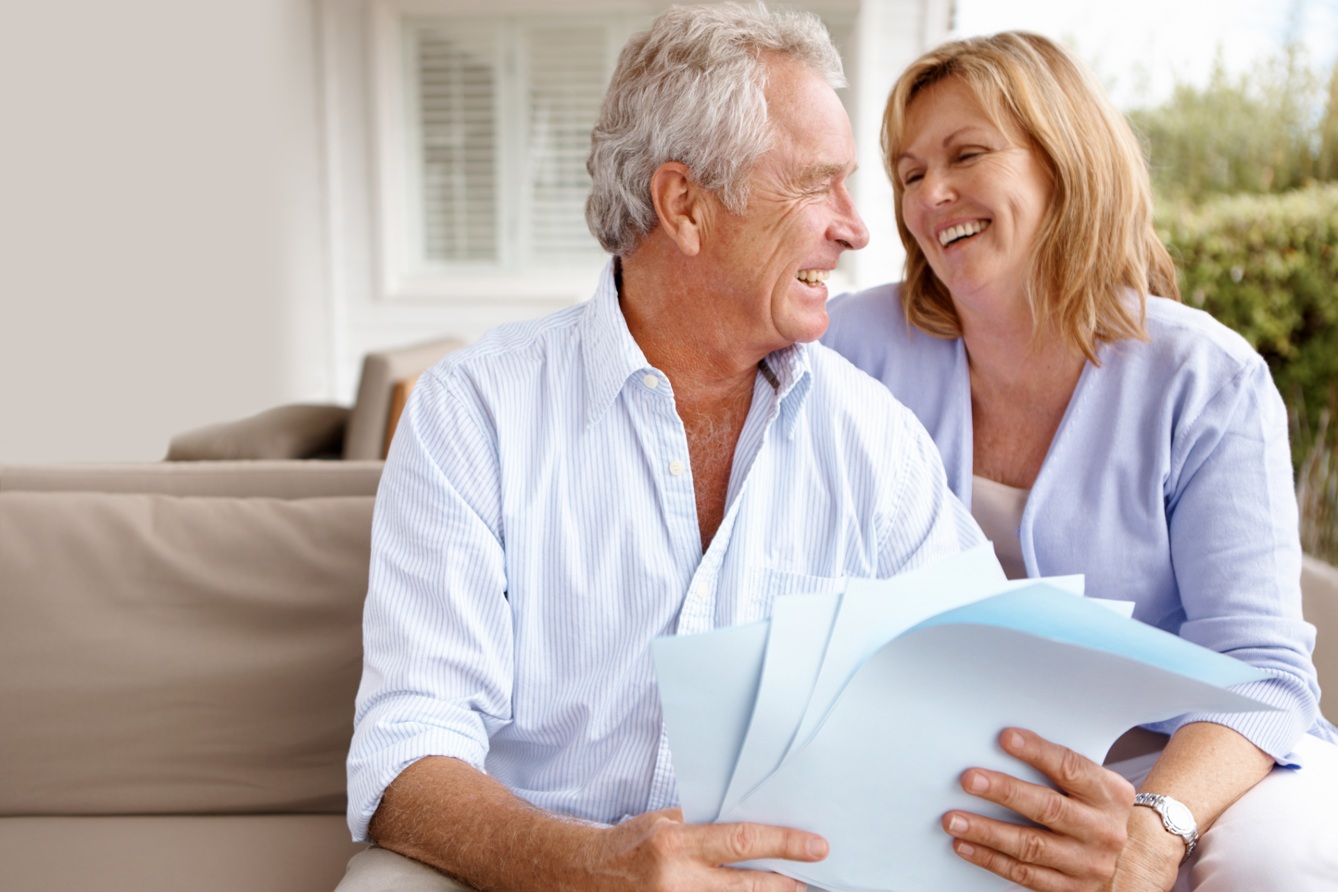 Woman showing tablet to smiling elderly couple, outdoors on a patio.