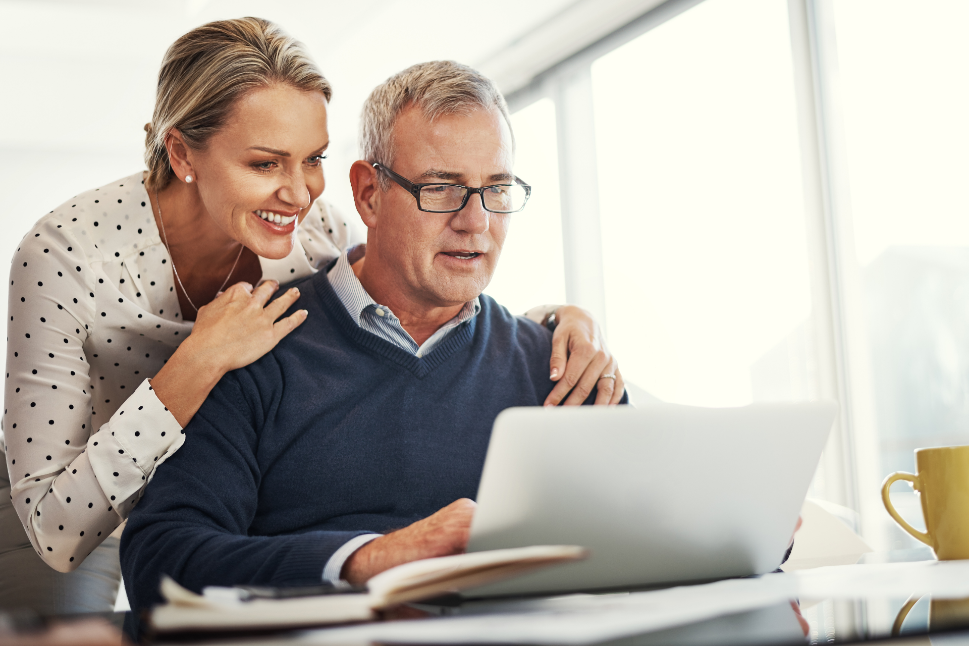 Woman with arms around a man, looking at a laptop together at a desk.