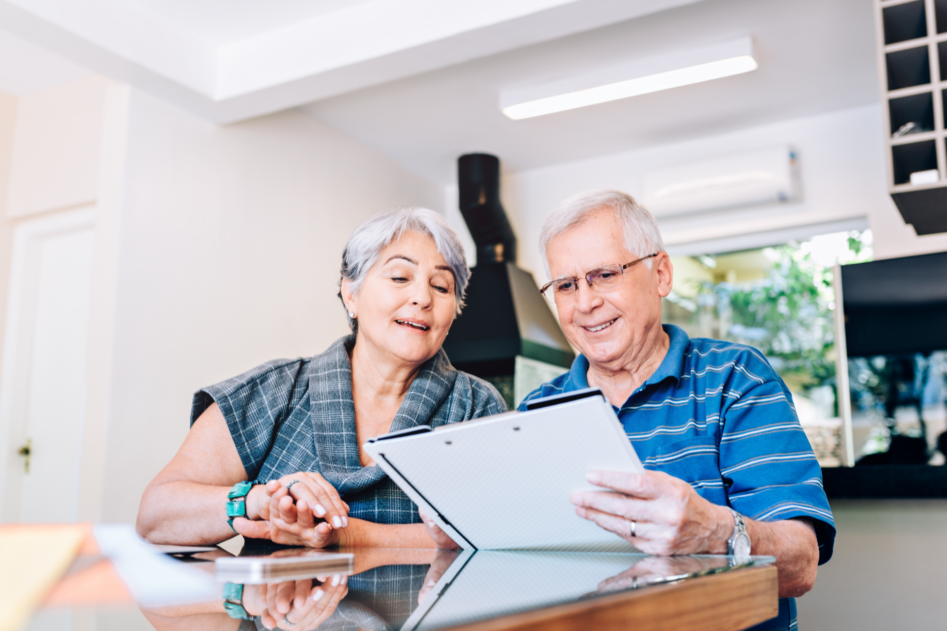 Older couple looking at a document on a clipboard together. They are smiling in a home setting.