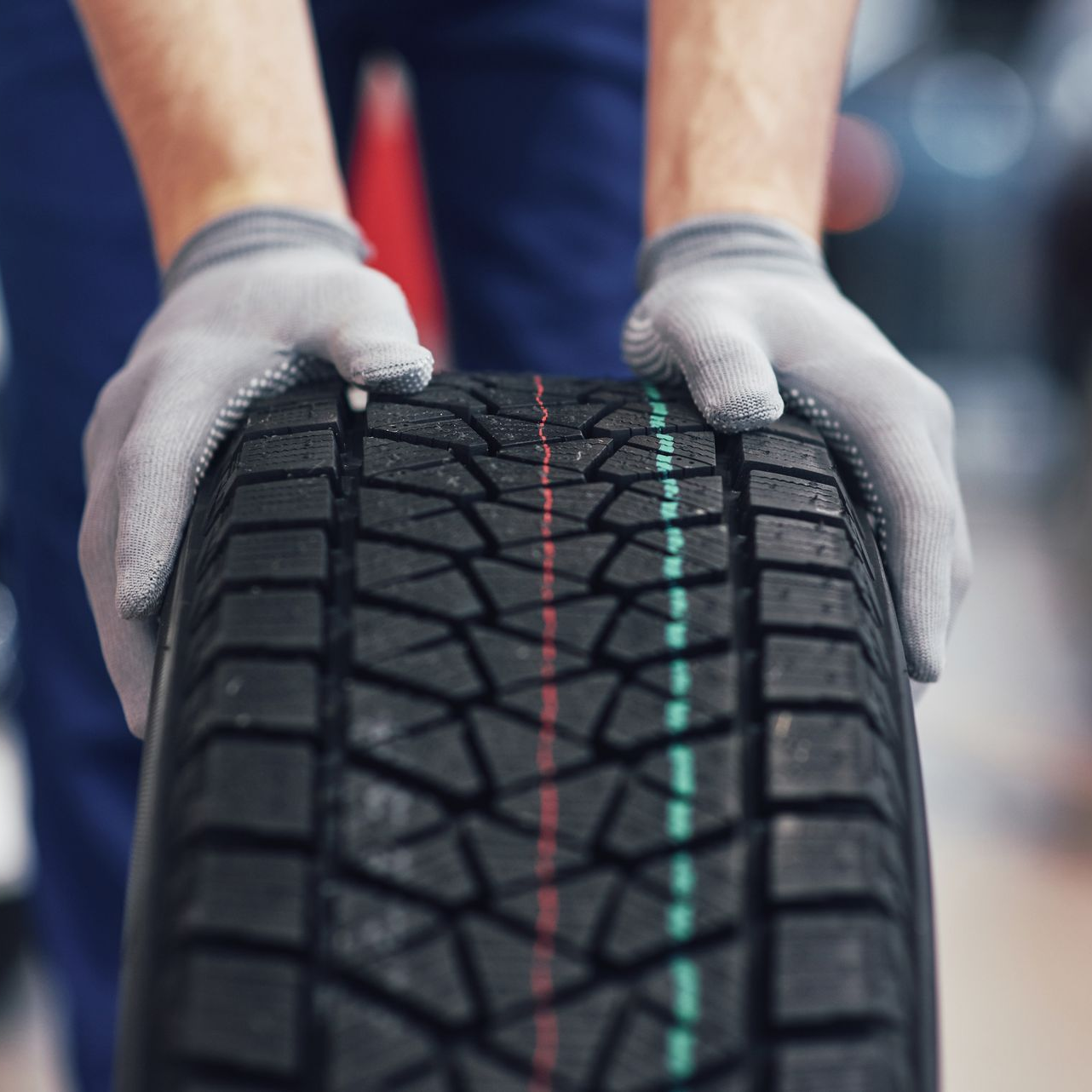 Person wearing gloves holding a tire with red and green tread lines.