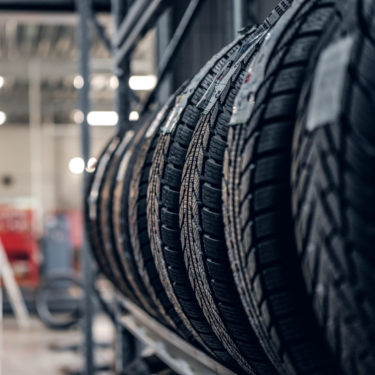 Tires stacked on a metal rack in a warehouse setting, with tread patterns visible.