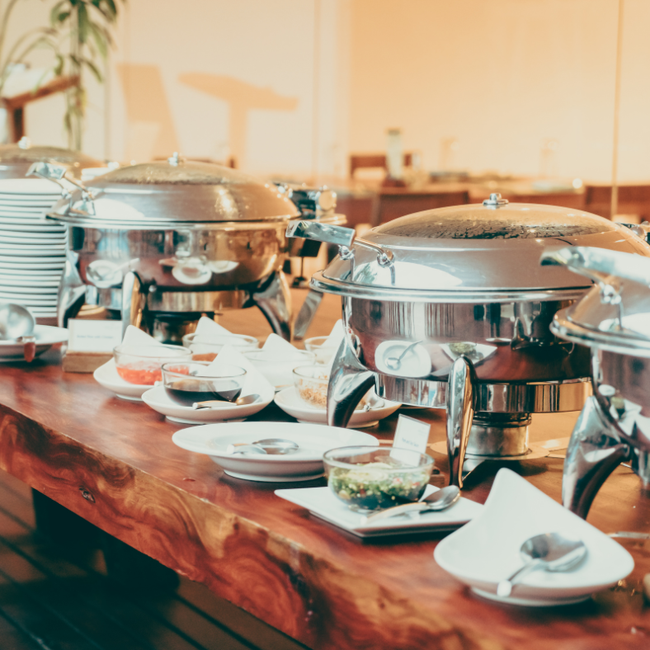 A buffet table with plates , bowls , and utensils on it.