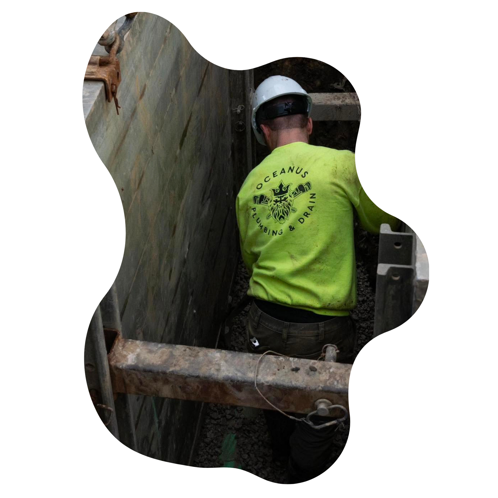 Worker in a white hard hat and neon green shirt standing in a narrow concrete trench.