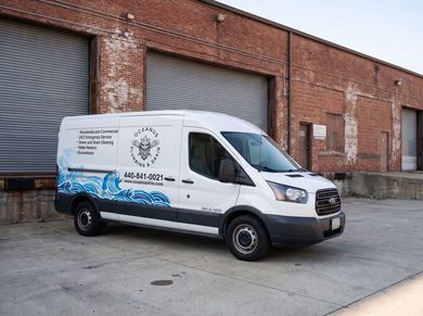 White utility van with blue wave graphics parked beside a road under a cloudy sky.