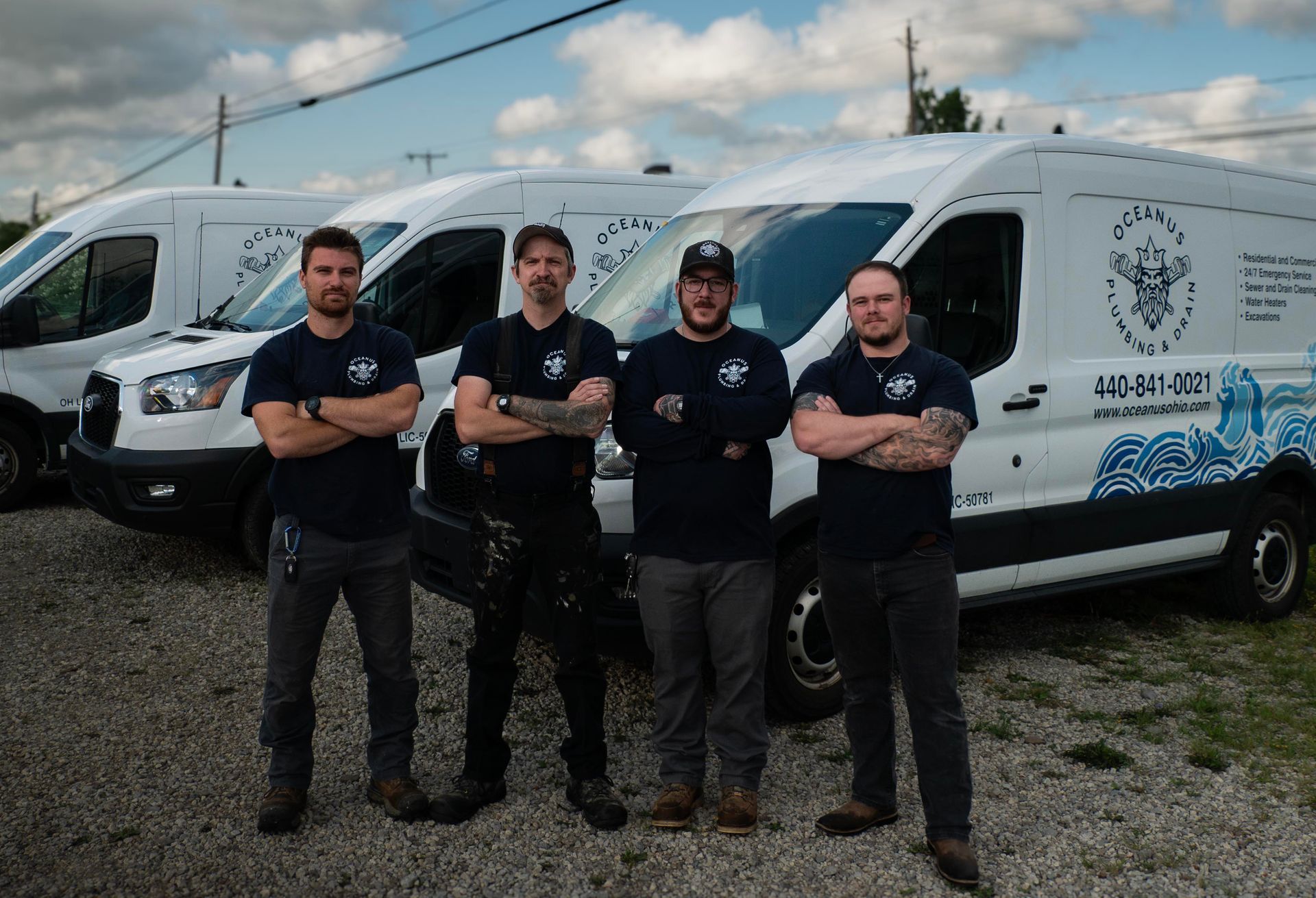 Four workers in dark shirts stand in front of white service vans outdoors, arms crossed.