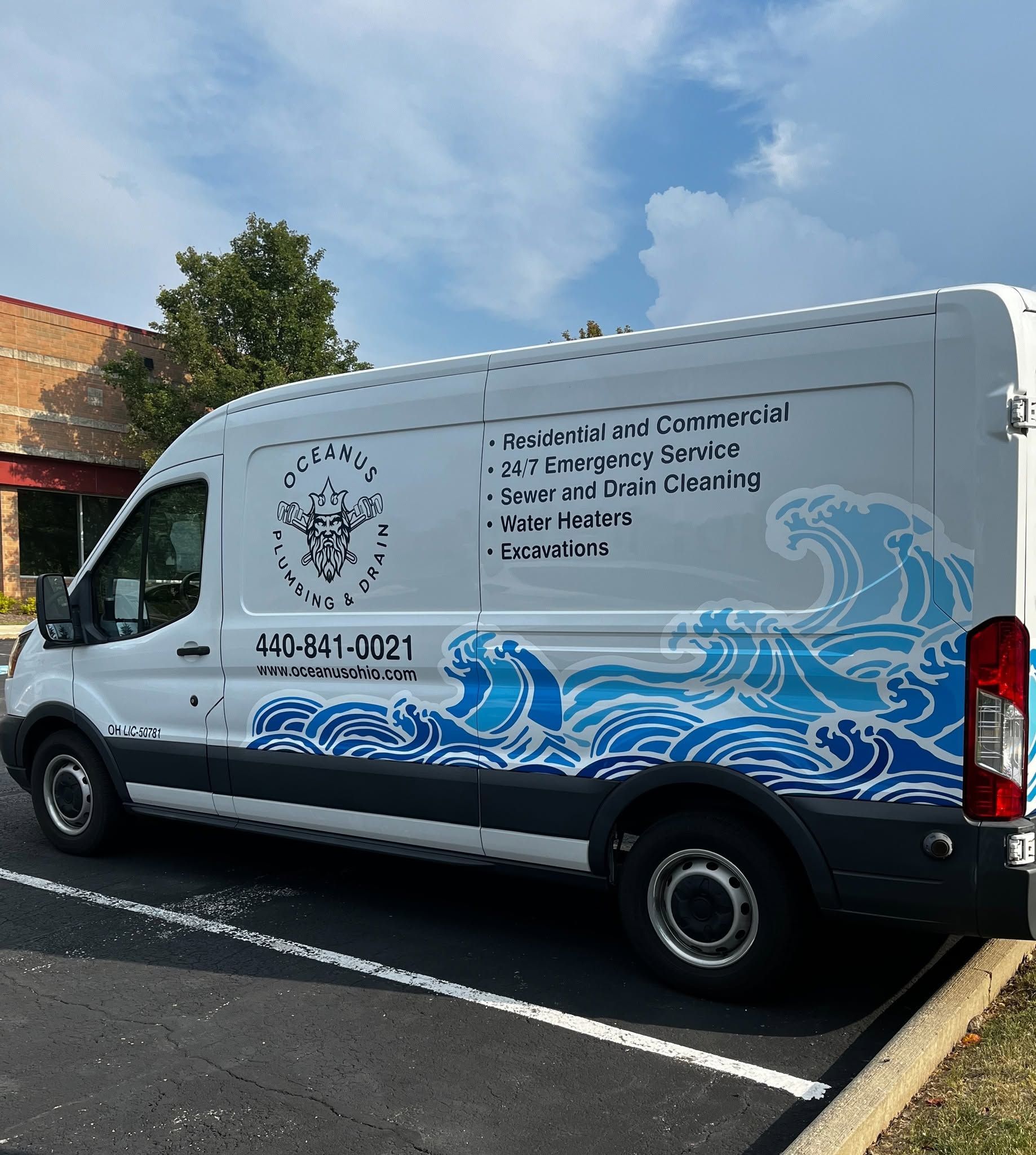 White utility van with blue wave graphics parked beside a road under a cloudy sky.