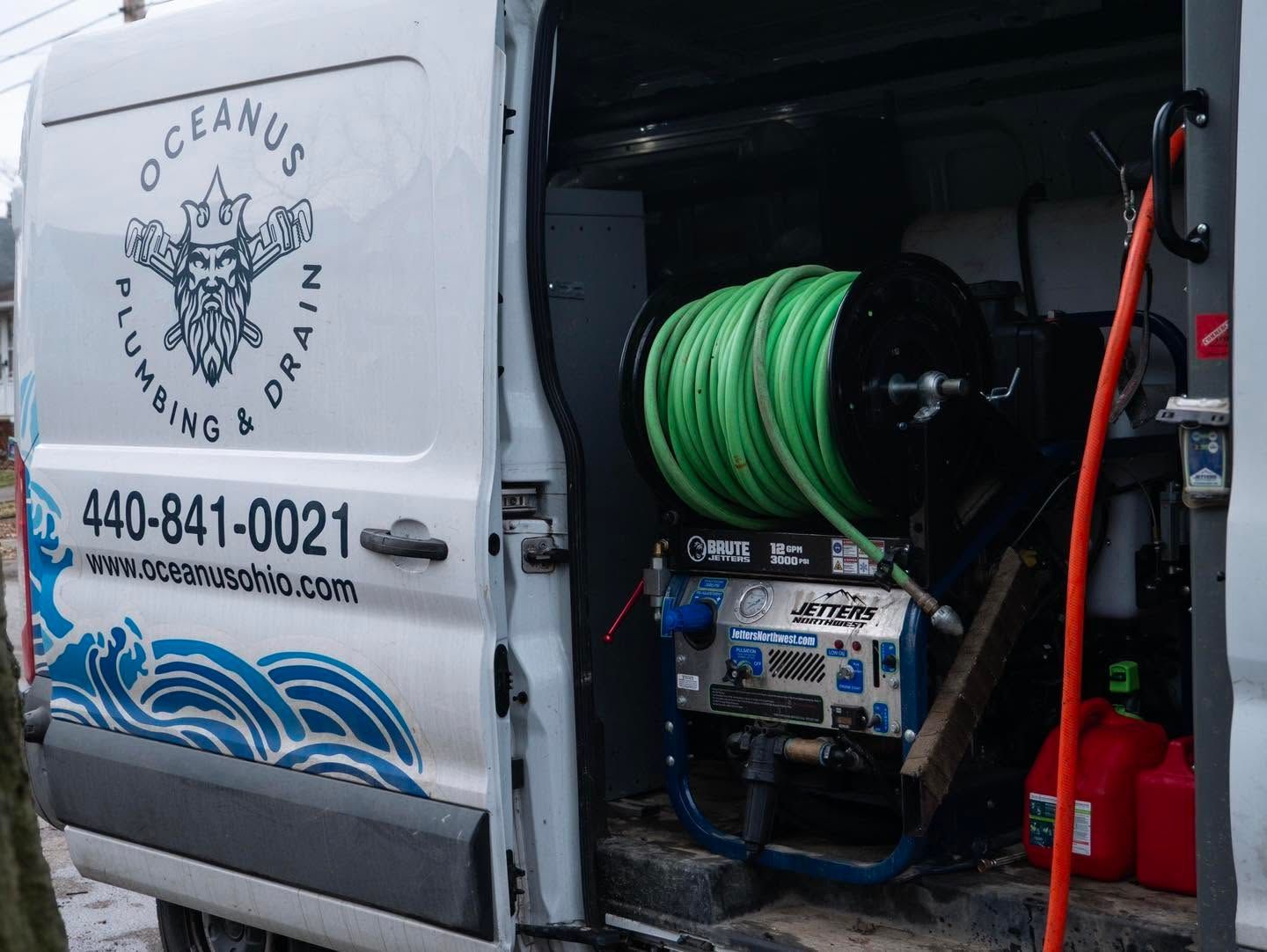 Service van with open side door showing green hose reel and equipment inside, “Oceanus Plumbing” logo on door.