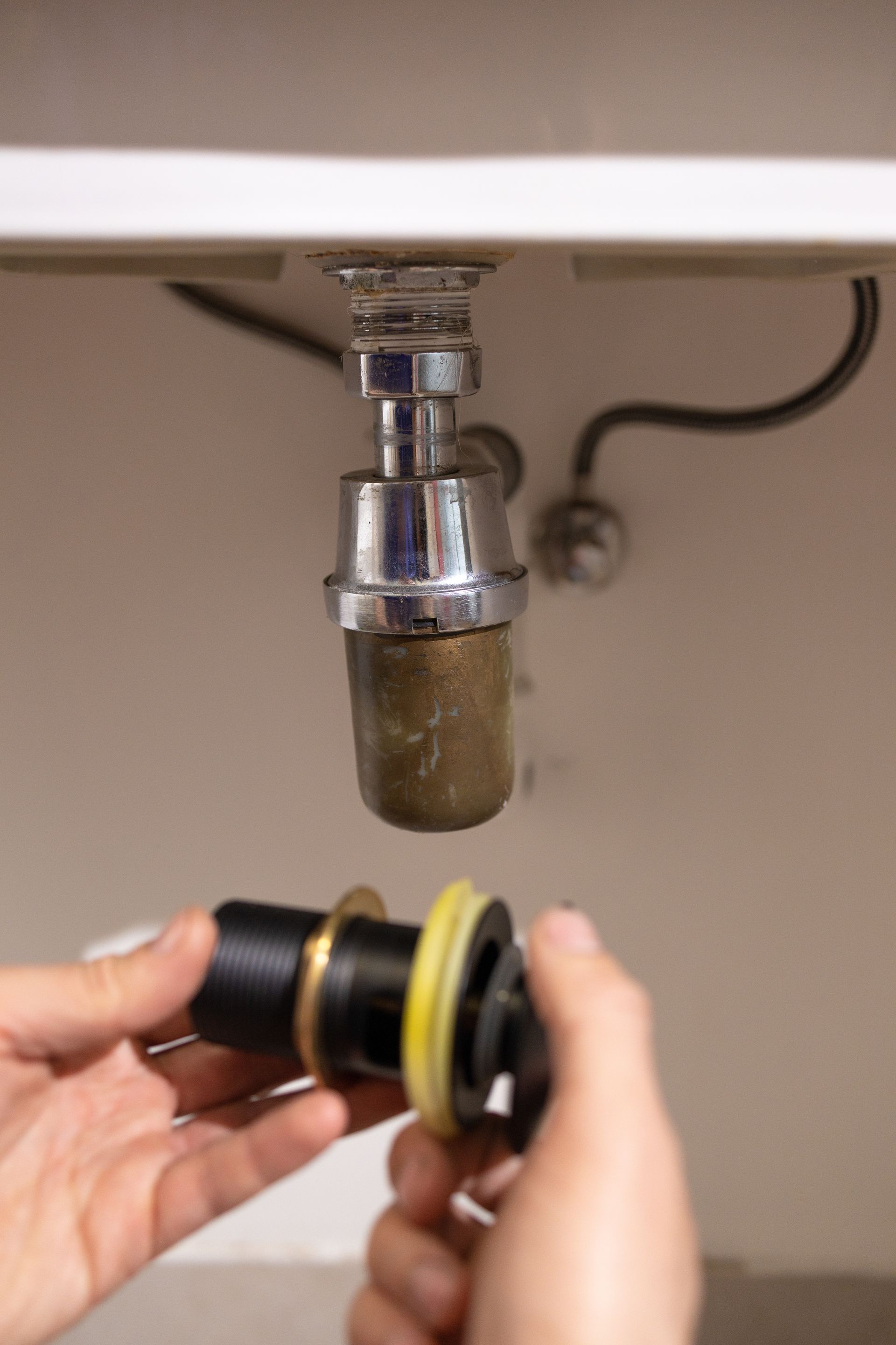 Hand holding a faucet aerator filter under a sink, with the sink drain and plumbing above.