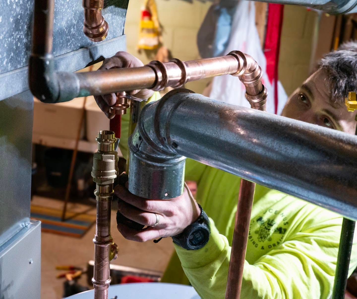 Person tightening copper pipes under a sink with a wrench in a utility space