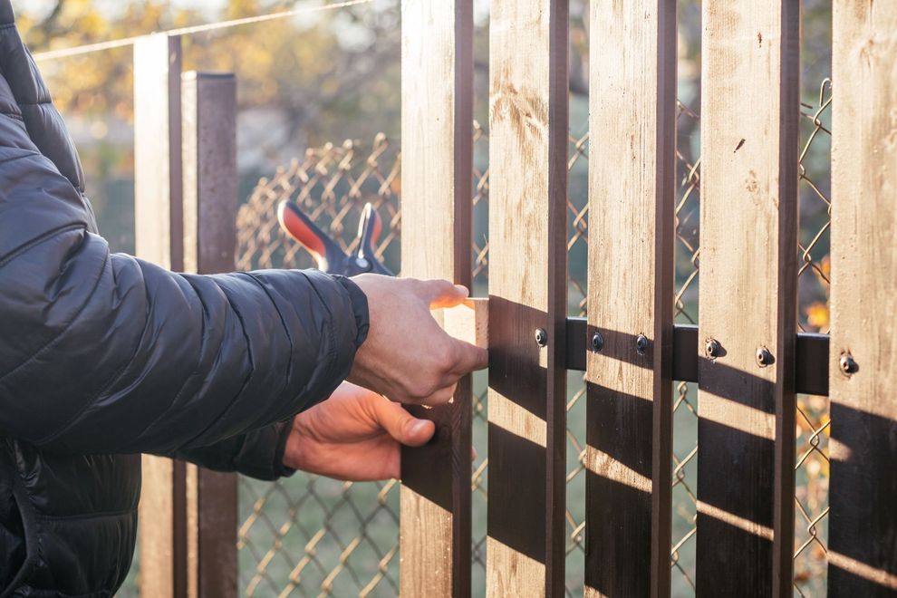 Hands unlocking a metal gate with a key and padlock