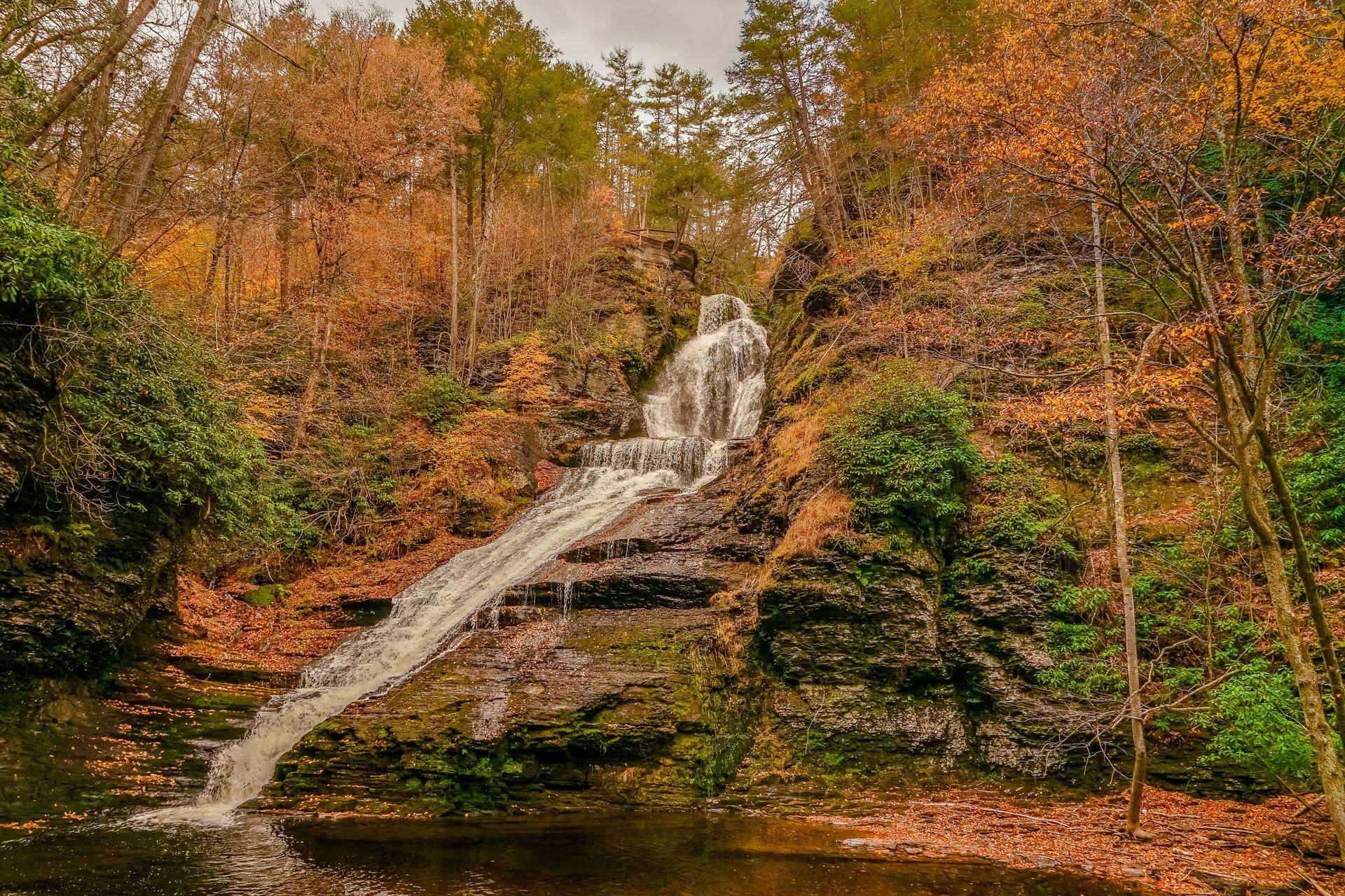 Autumn waterfall cascading over rocks amid orange and green forest foliage