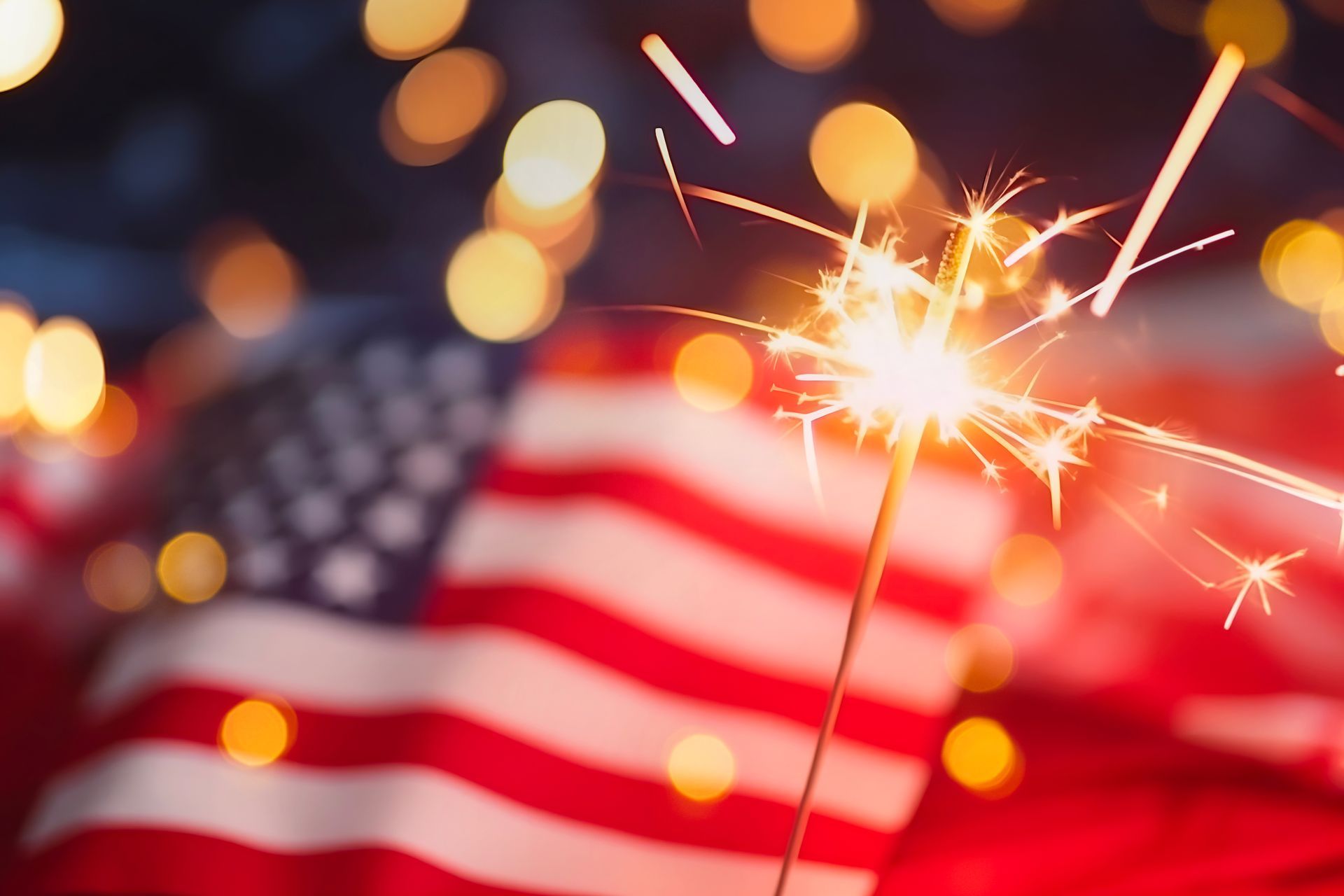 American flag with a lit sparkler and warm bokeh lights in the background