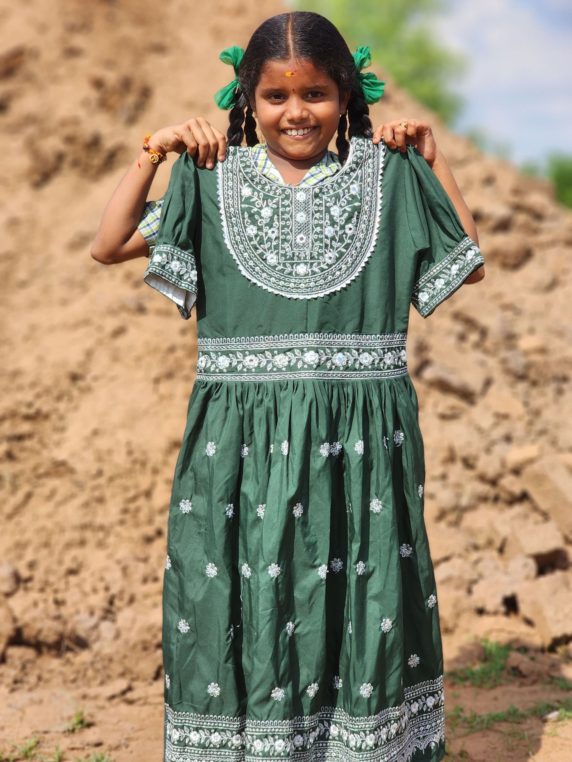 A little girl in a green dress is standing in front of a pile of dirt
