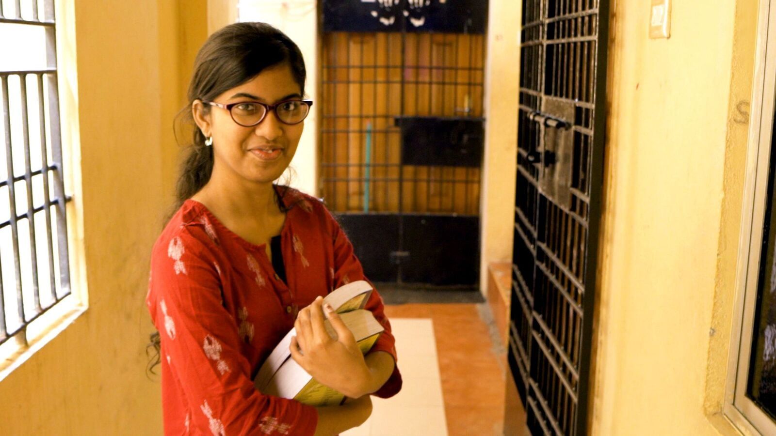 A young woman is standing in a hallway holding a book.