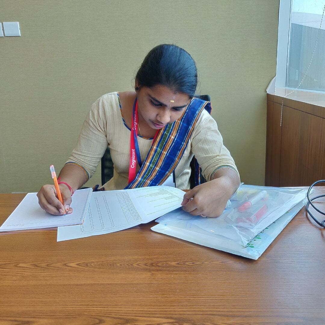 A woman is sitting at a desk writing on a piece of paper.
