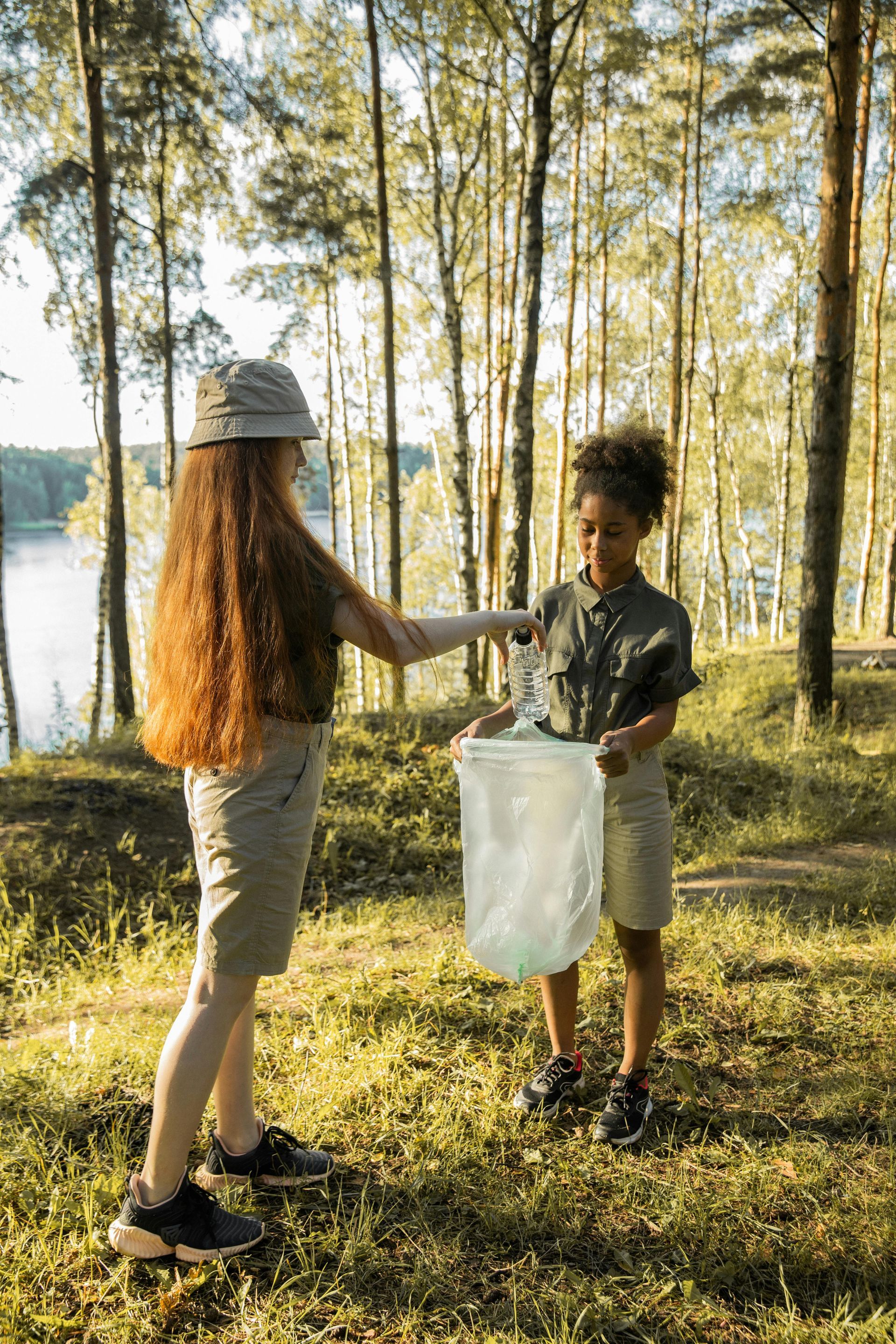 A boy and a girl are picking up trash in the woods.