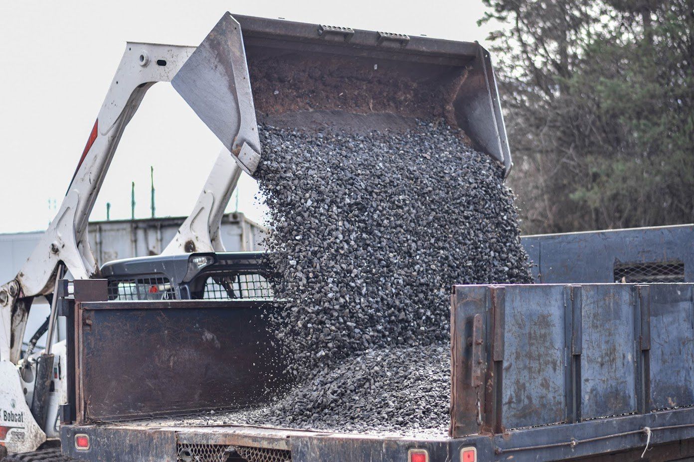 Skid steer loader unloading gravel aggregate into a dump truck