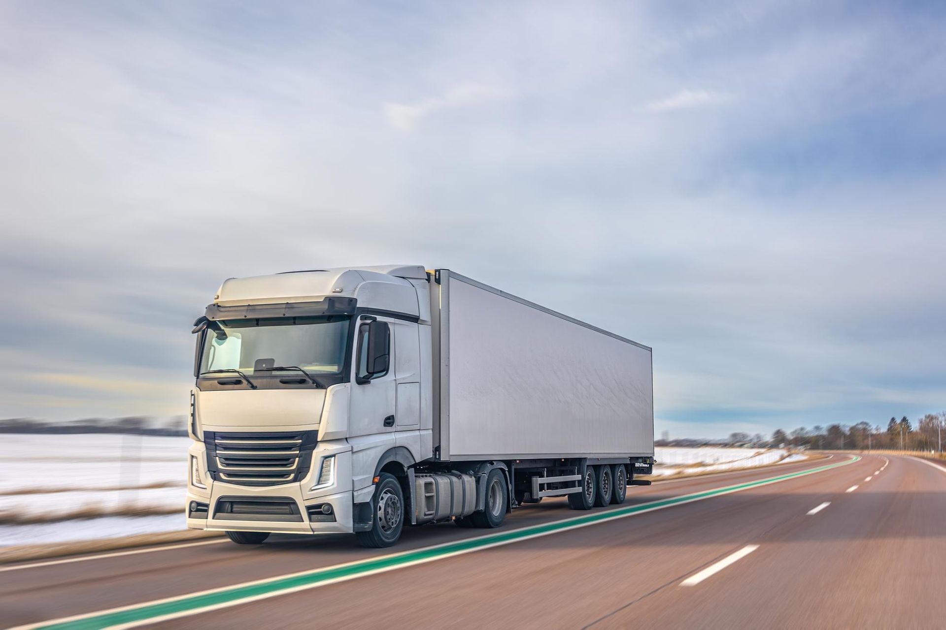 White semi-truck driving on a highway under a cloudy sky