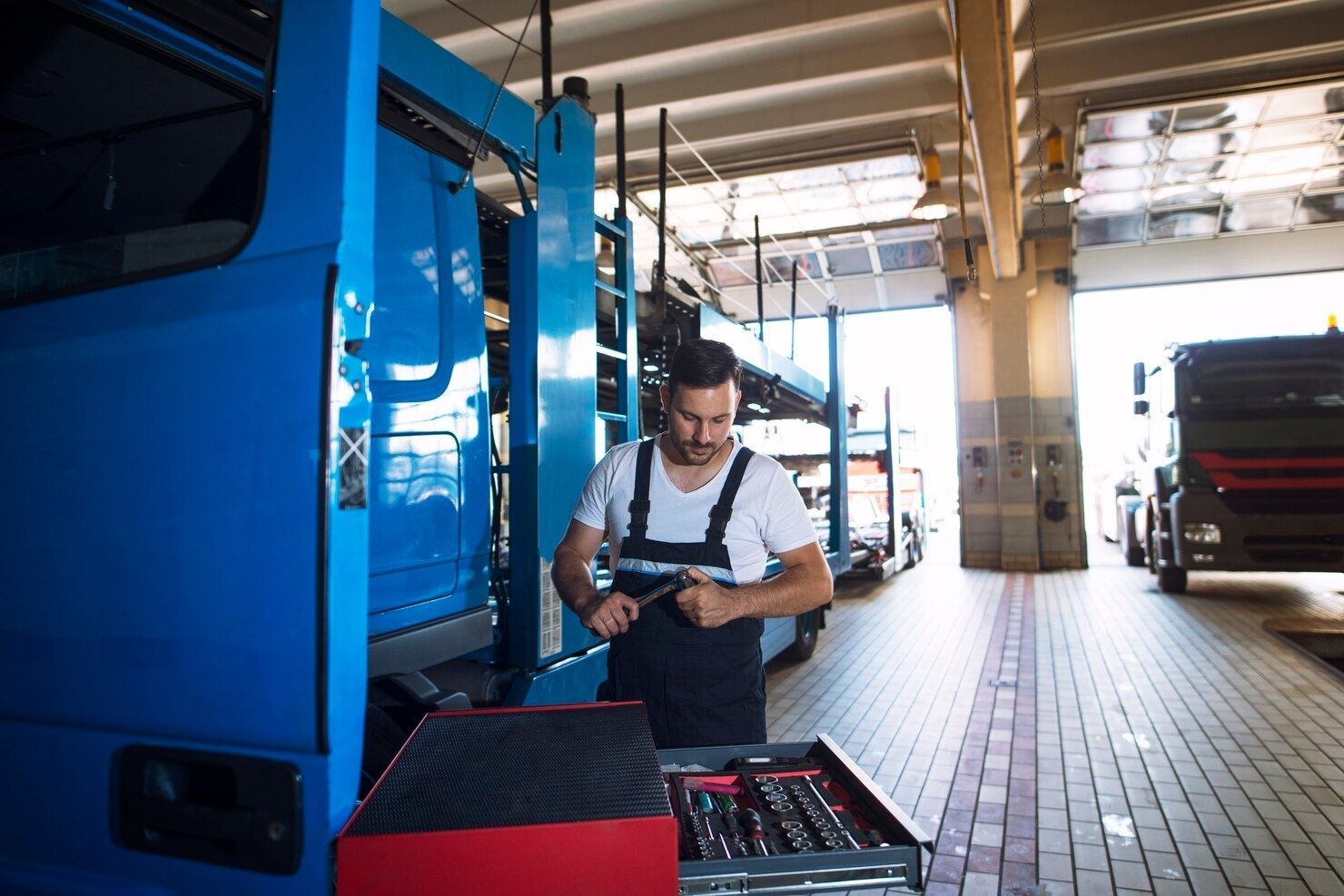 Mechanic checking tools beside a blue truck inside a garage bay