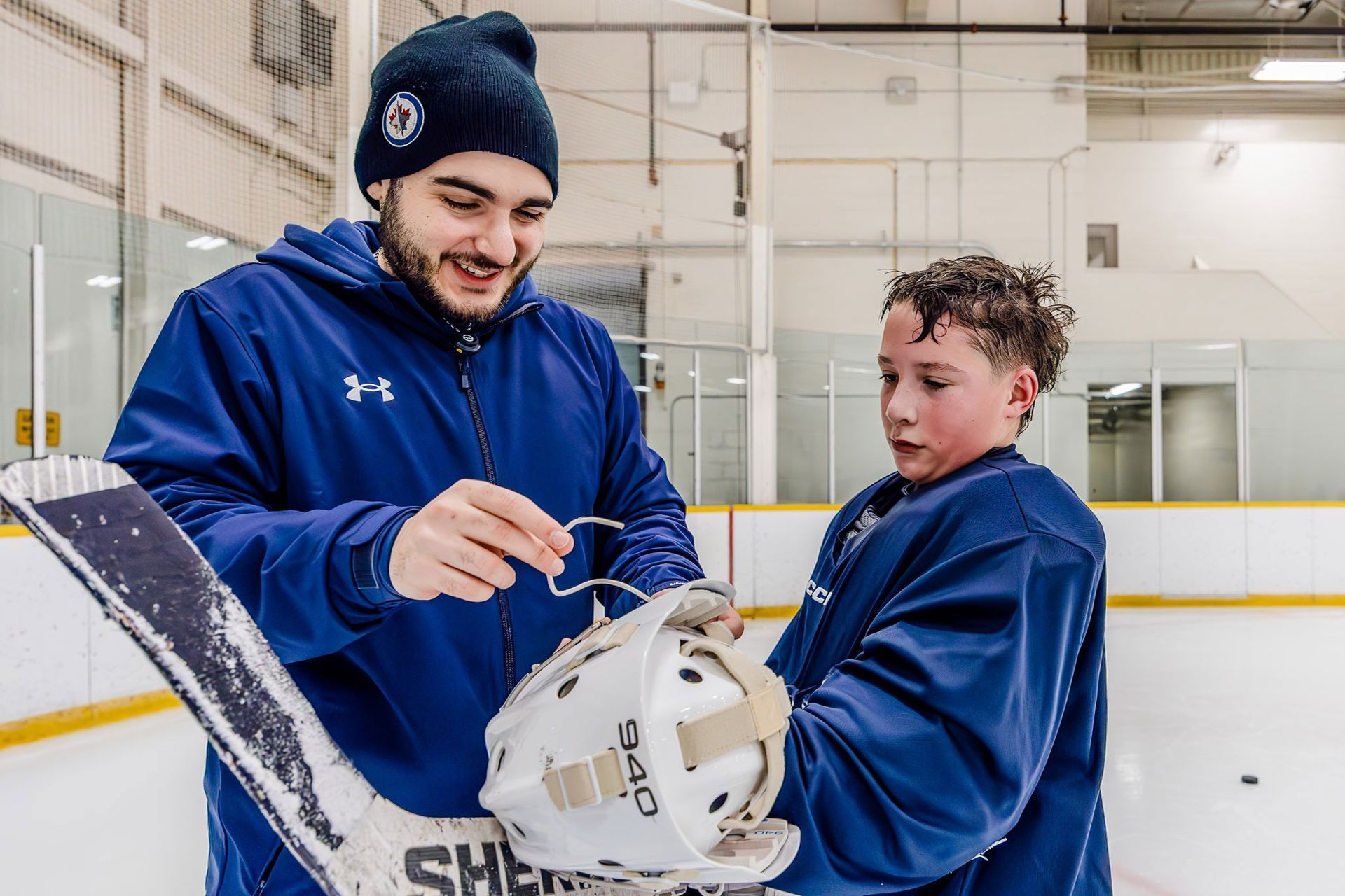 Coach showing a youth hockey player how to hold a stick on an ice rink