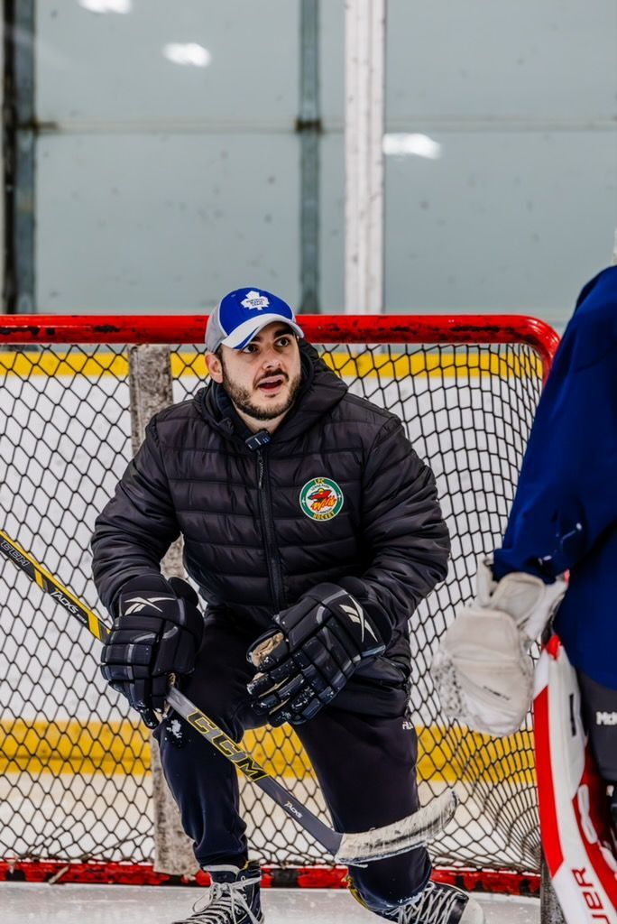 Hockey goalie in black gear and blue cap sits in front of the net during practice.