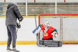 Adult in winter clothing coaching a child goalie in a small hockey net on an ice rink