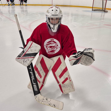 Ice hockey goalie in red jersey and white pads crouching on the rink
