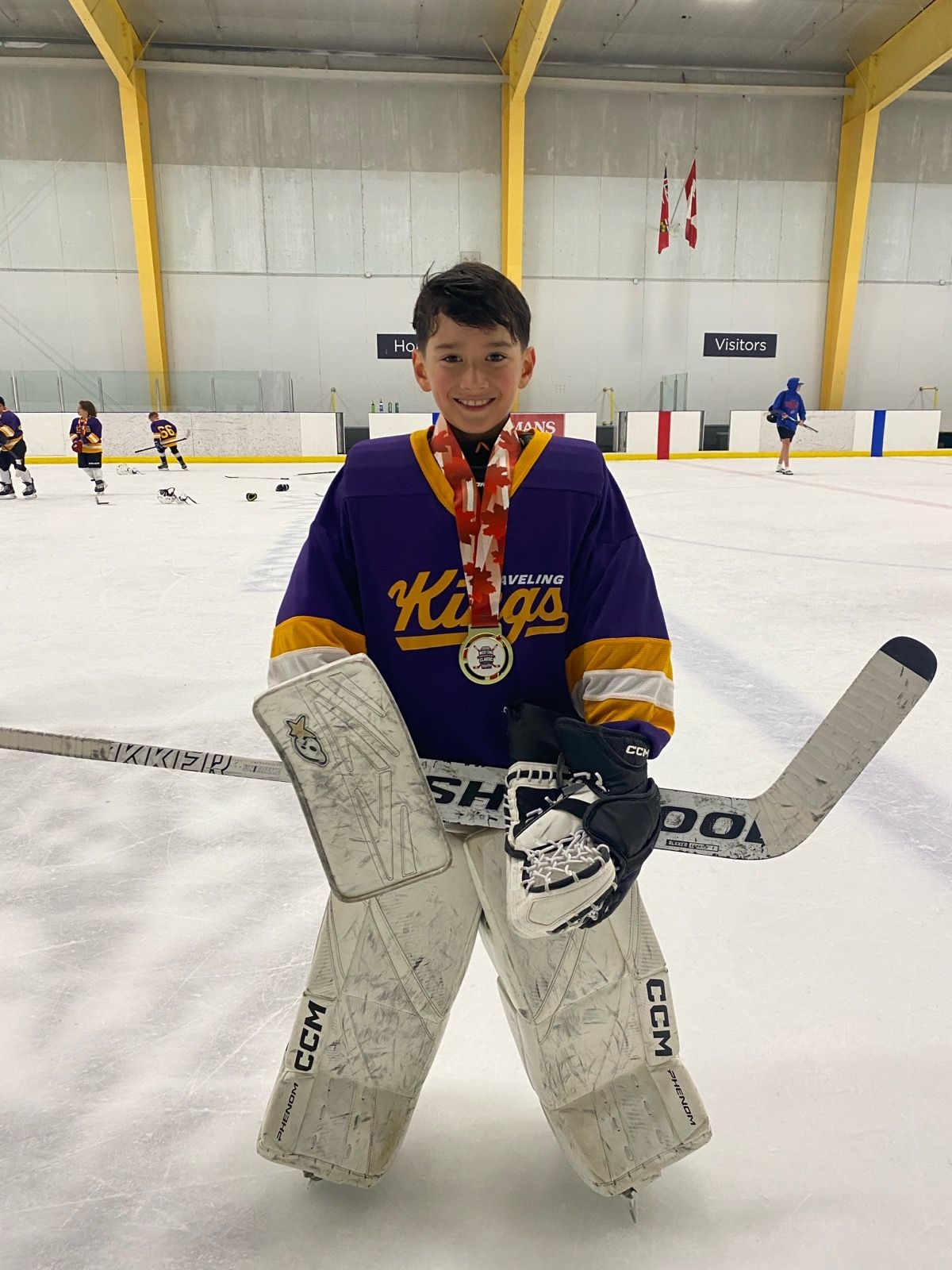 Youth hockey goalie in purple Kings jersey posing on the ice with goalie pads and medal.