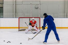 Hockey practice: blue-clad player shoots at a red-jersey goalie in an indoor rink