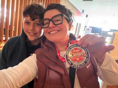 Two people smiling indoors, one holding up a Playoffs Finals medal