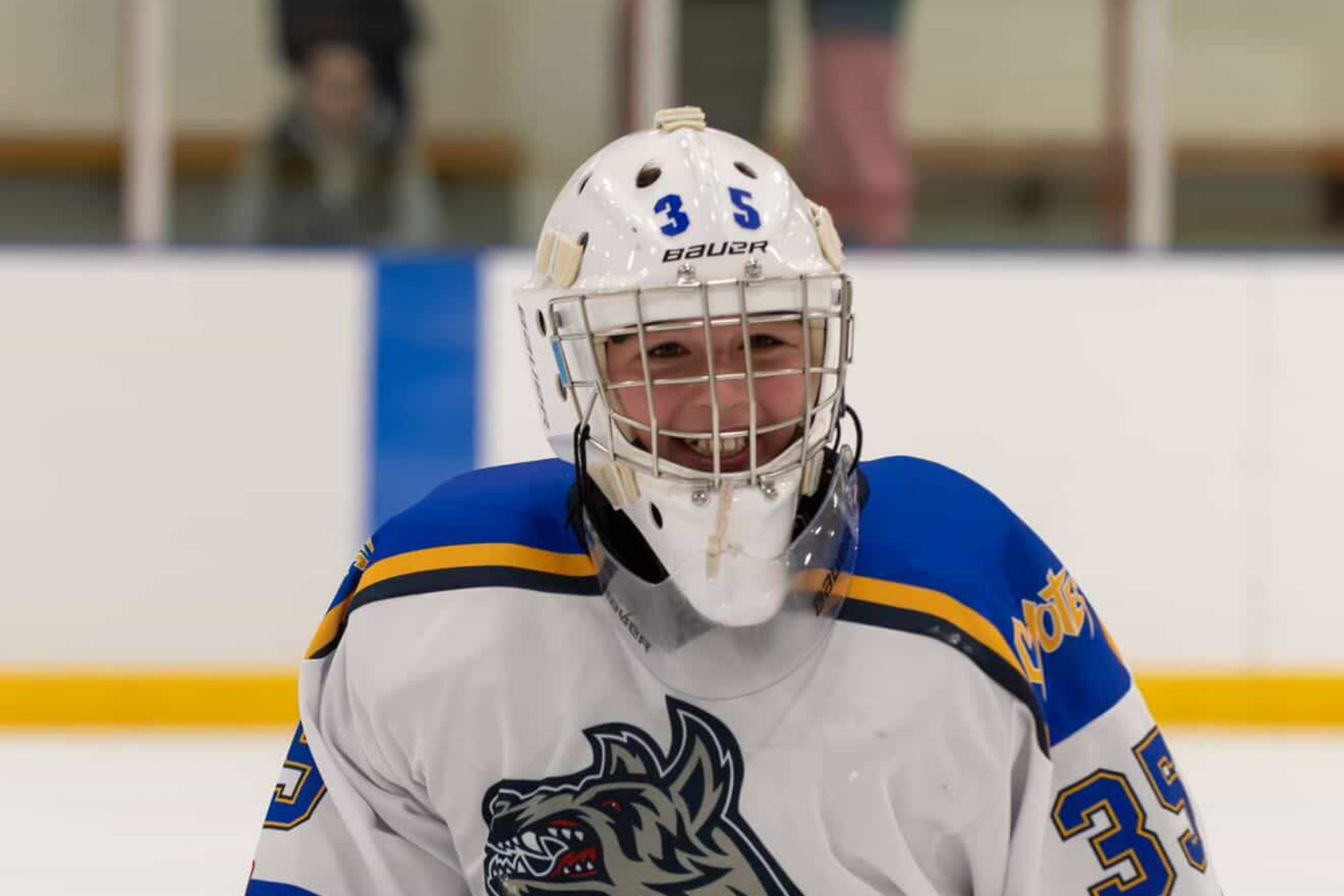 Hockey goalie in white and blue jersey and helmet on the ice, facing forward