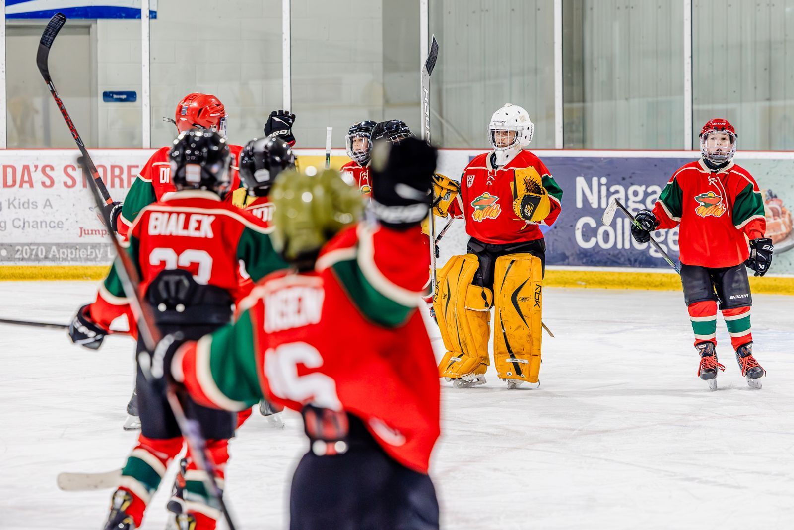 Youth ice hockey players in red jerseys gather on the rink during a game break