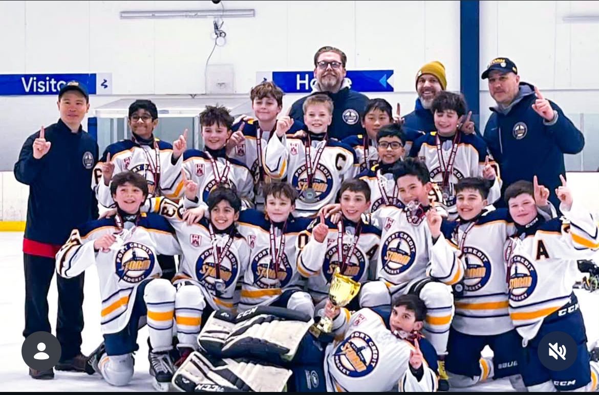 Youth hockey team and coaches posing in white jerseys with a championship trophy on the ice.