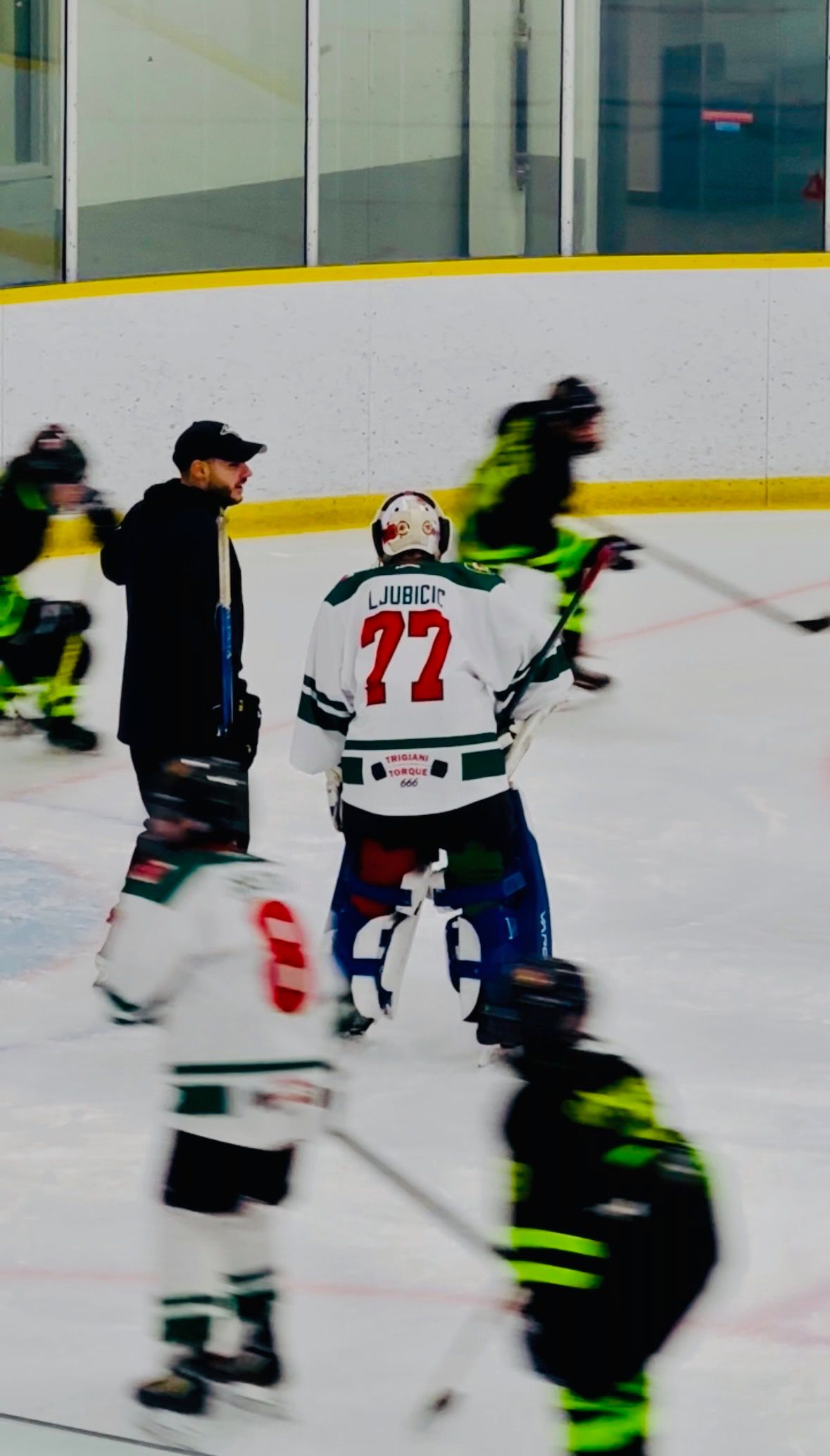 Ice hockey players in black and white jerseys skate near the boards during a game