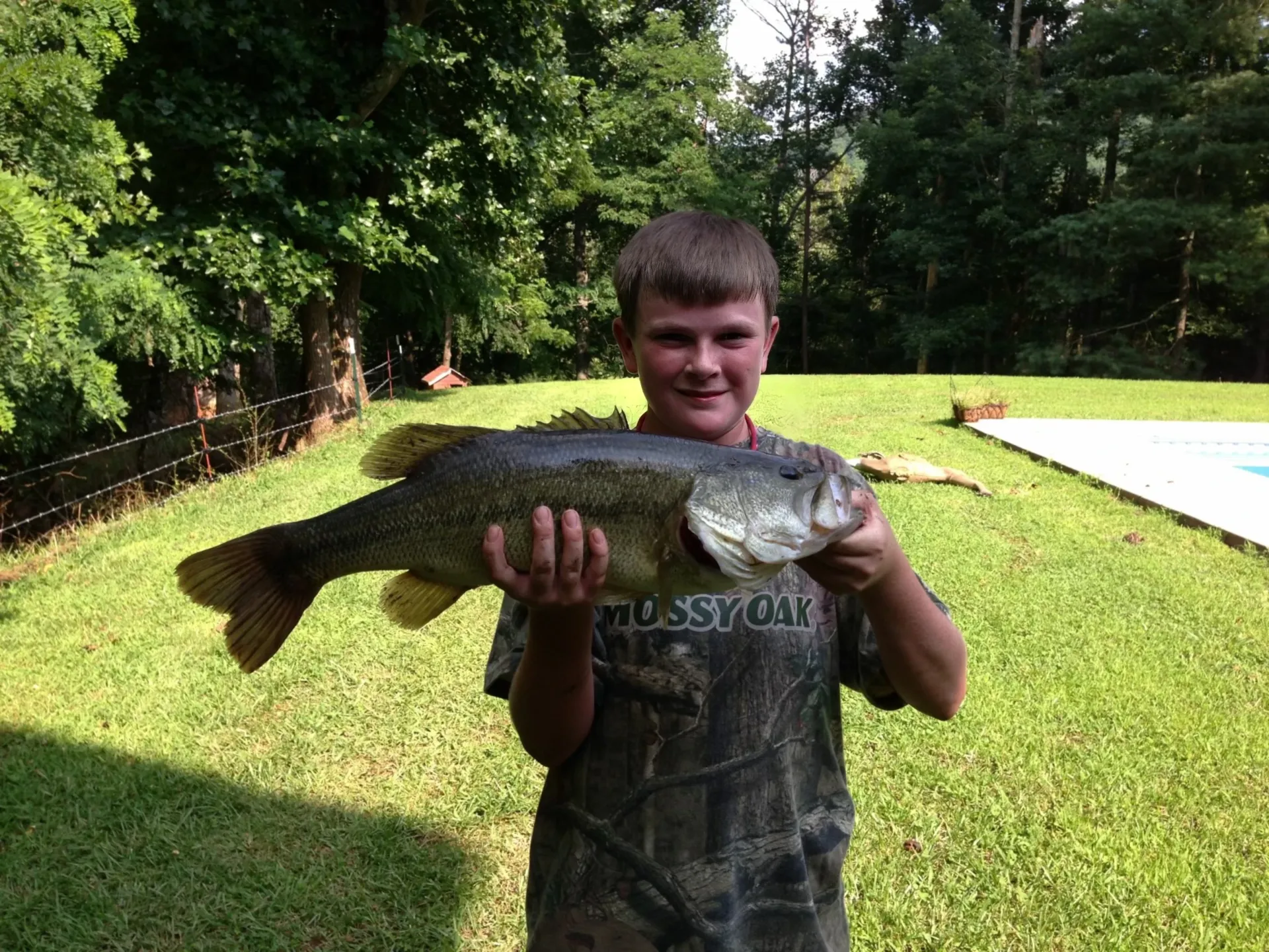 A young boy is holding a large fish in his hands.