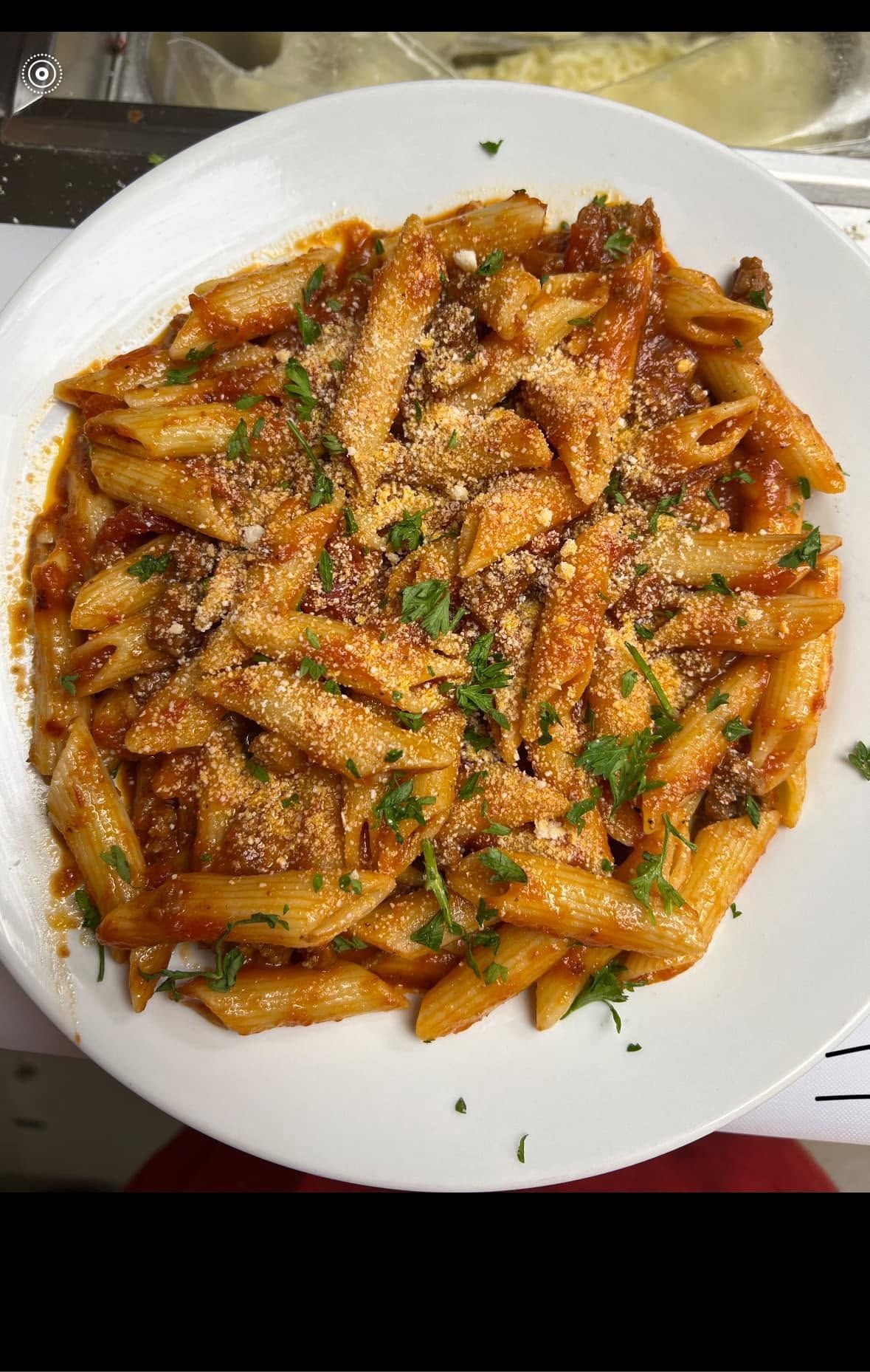 Plate of penne pasta in red sauce, garnished with herbs, on a white plate.