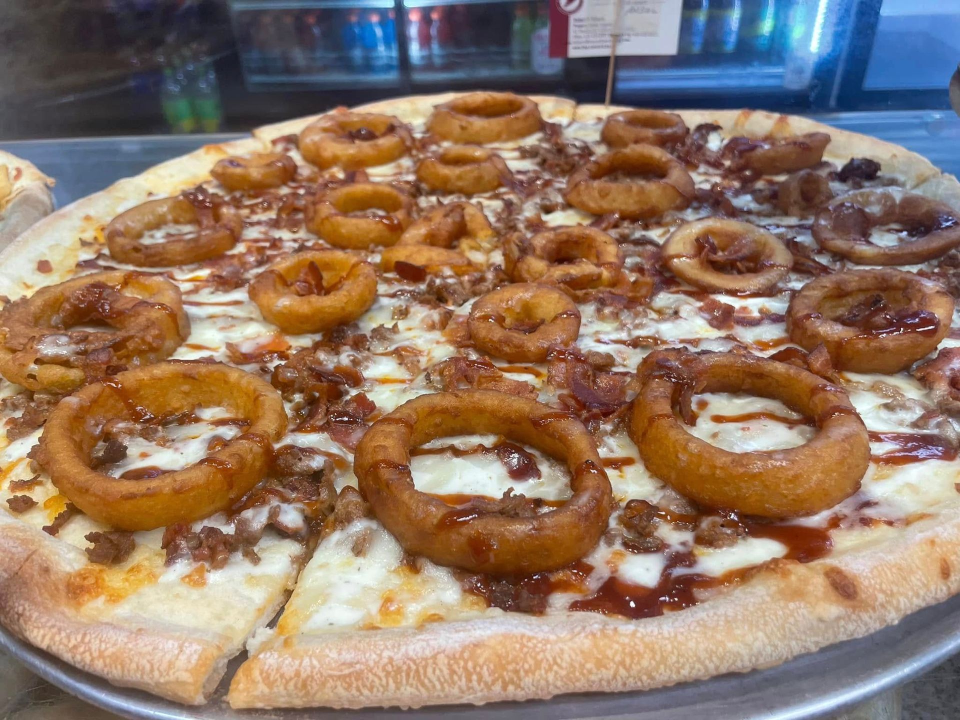 Large pizza topped with onion rings and barbecue sauce on a tray