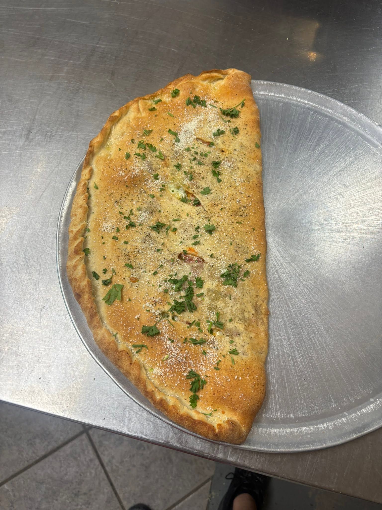 Half-moon folded omelet on a plate, garnished with herbs on a metal countertop
