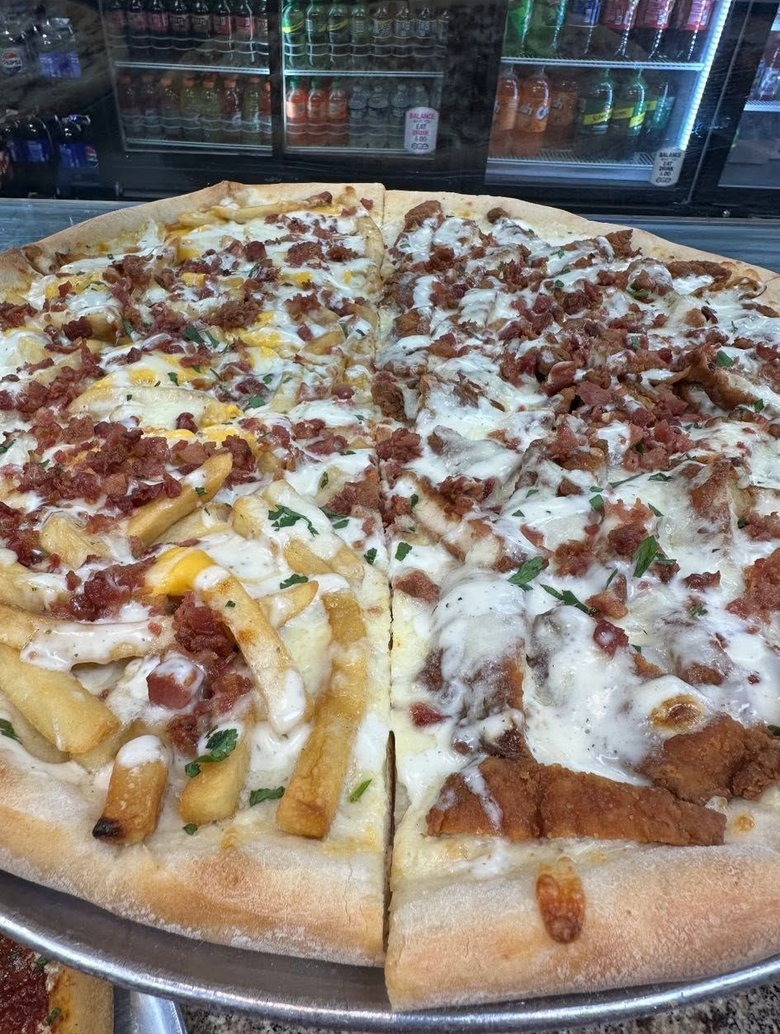 Split pizza topped with cheese and fries on a metal tray in a restaurant fridge display.