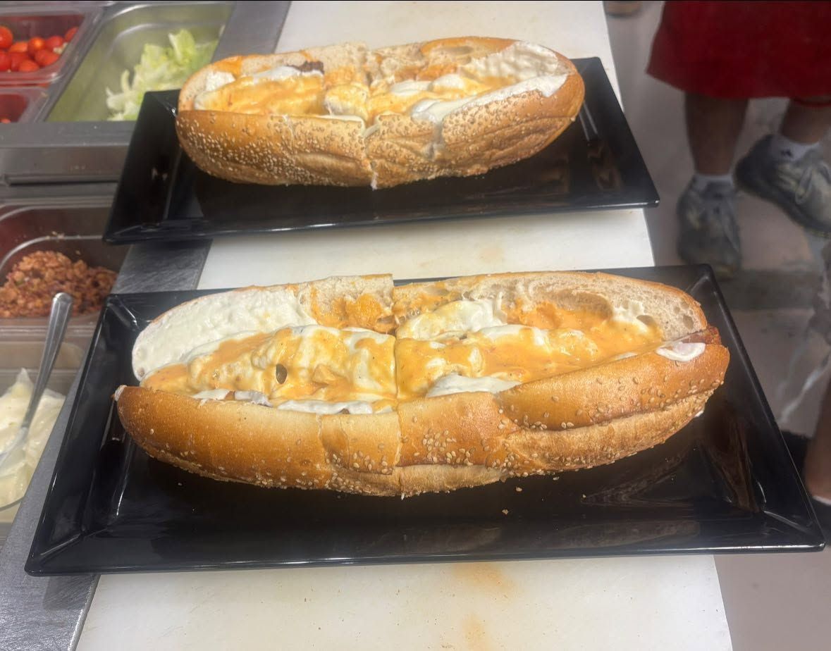 Two baked loaves topped with sugar on black trays at a bakery counter