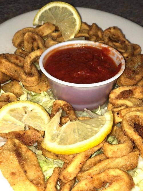 Fried seafood rings with lemon wedges around a cup of red marinara sauce