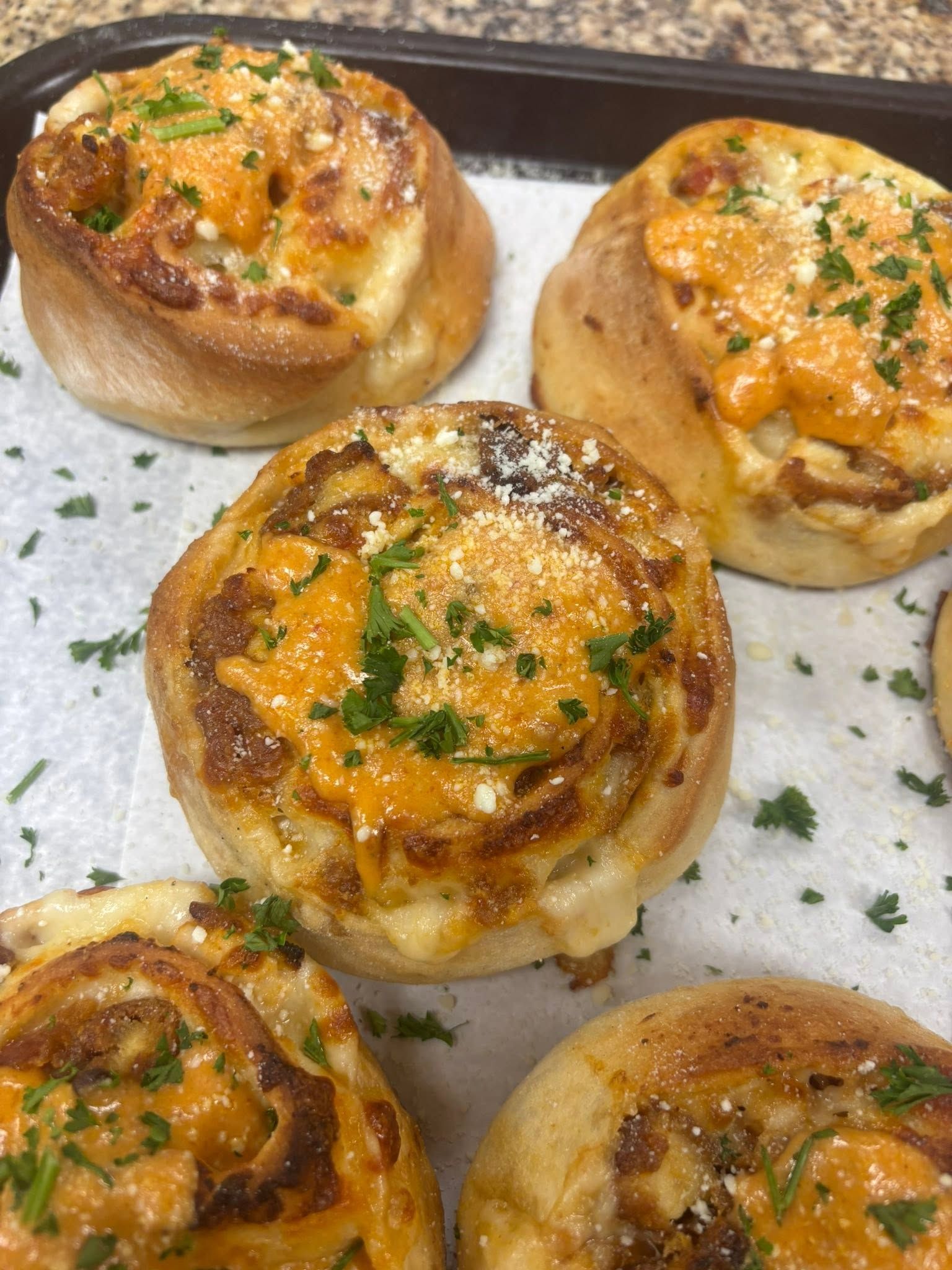 Five cheesy baked rolls on a tray, topped with herbs and orange sauce