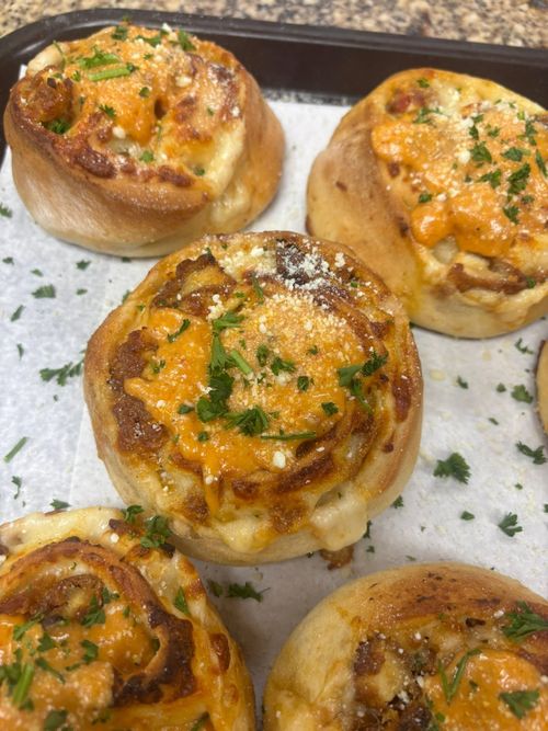 Five cheesy baked rolls on a tray, topped with herbs and orange sauce