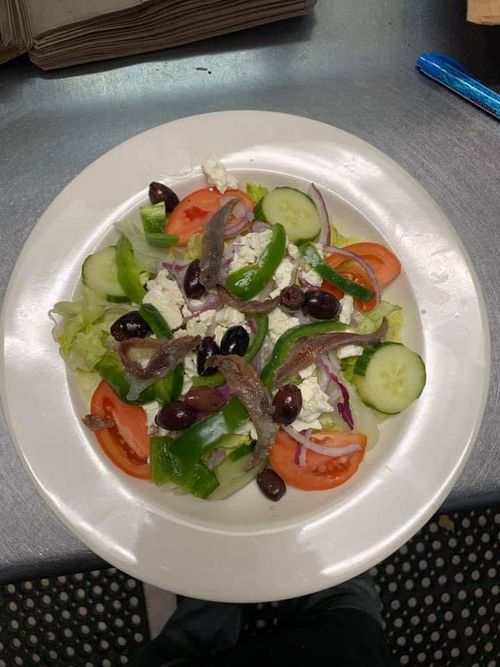 Greek salad on a white plate with lettuce, tomatoes, cucumbers, olives, onions, and feta at a table