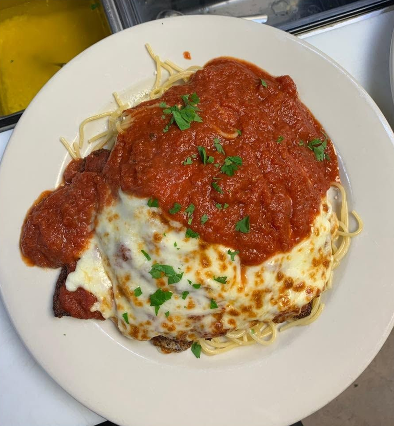 Plate of spaghetti topped with red marinara and melted cheese, garnished with parsley