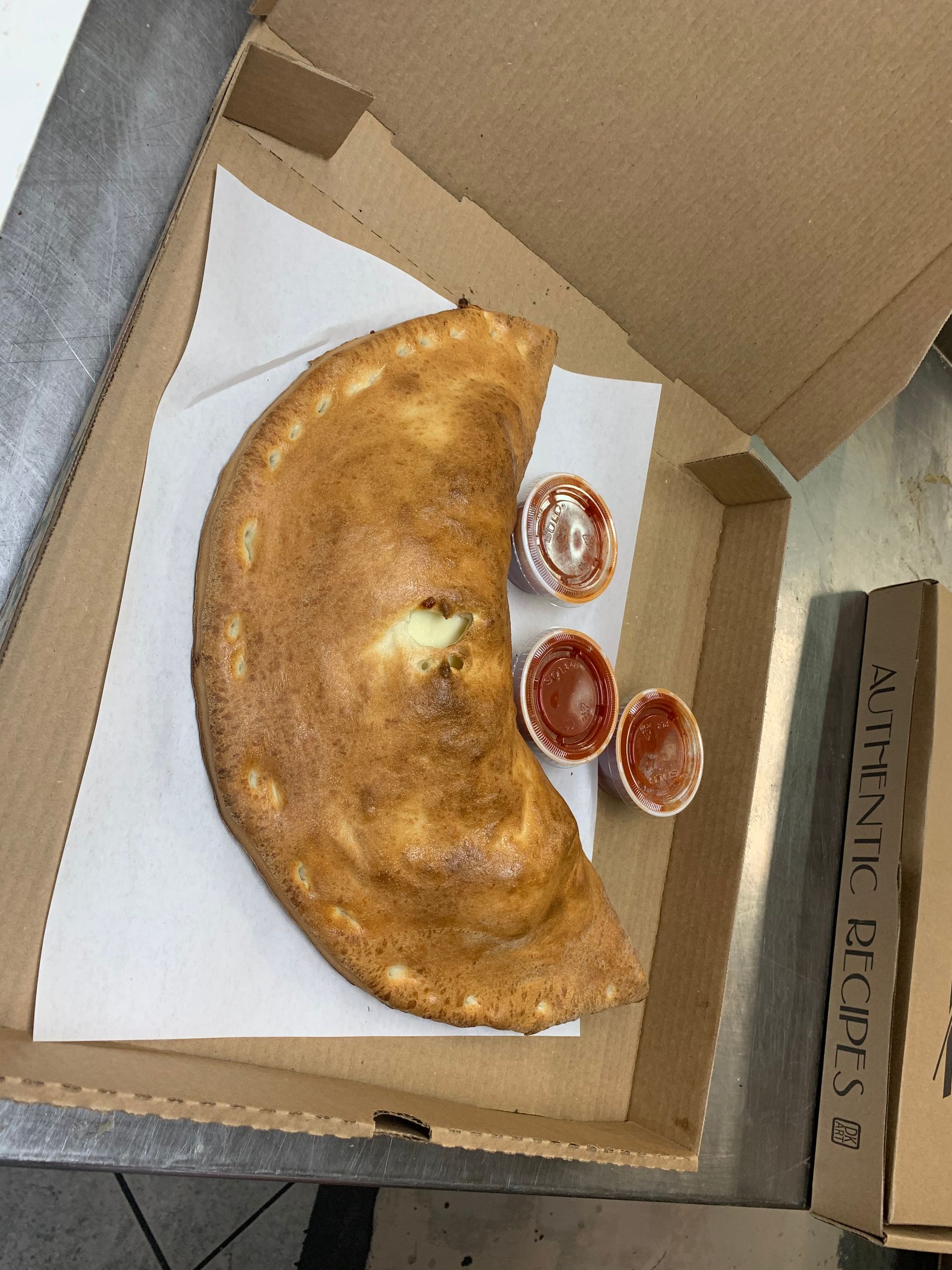 Open pizza box with a half-eaten calzone and three dipping sauce cups inside