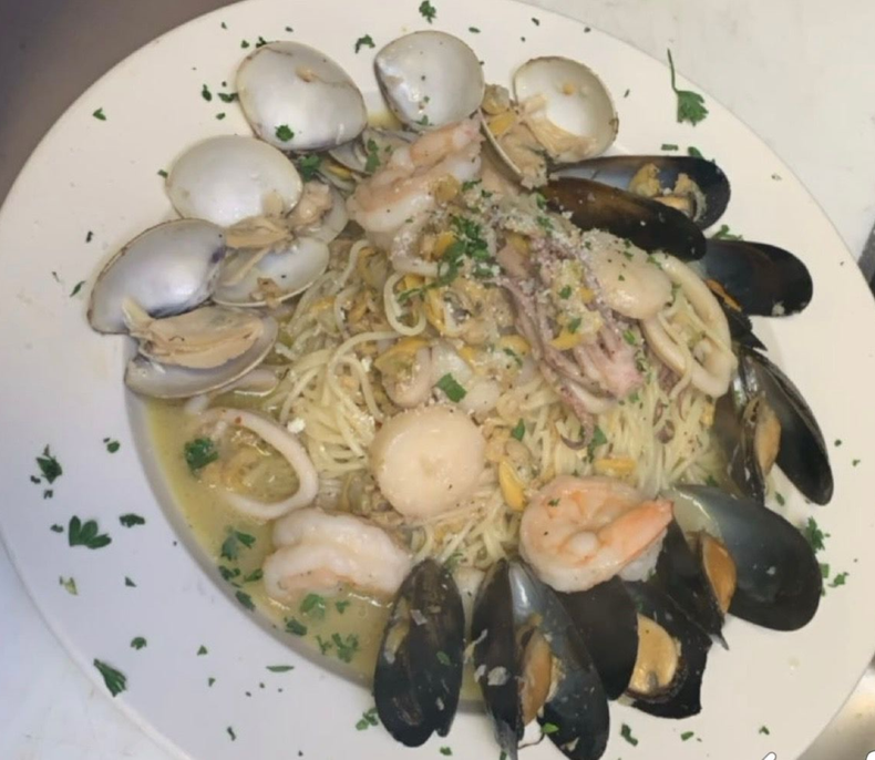 Seafood pasta with clams, mussels, shrimp, and parsley on a white plate